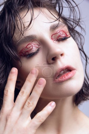 Nahaufnahme Porträt eines jungen schönen Mädchens mit nassen Haaren, rotem String-Make-up auf den Augenlidern. Revolutionäre Hautpflege. Konzept moderner Schönheitsstandards, plastische Chirurgie, Gesundheit, Kosmetologie