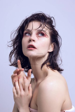Anti-aging cosmetological treatment. Portrait of young elegant woman with bare shoulders, wet messy hair and red tangled strings on eyes. Beauty standards, plastic surgery, health, cosmetology concept