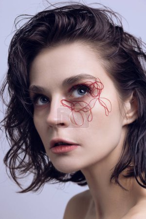 Portrait of beautiful young woman with deep blue eyes, red tangled strings on eyes and wet messy hair. Face lifting, treatment. Concept of modern beauty standards, plastic surgery, health, cosmetology