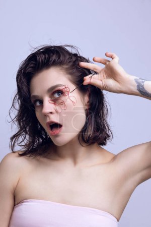 Young beautiful woman with red tangled strings and needle close to face. Changing facial look, beauty treatment. Concept of modern beauty standards, plastic surgery, health, cosmetology