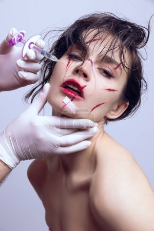Foto de Mujer joven con arañazos en la cara haciendo inyección facial en clínica cosmetológica. Rellenos en la cara. Concepto de estándares modernos de belleza, cirugía plástica, salud, cosmetología - Imagen libre de derechos