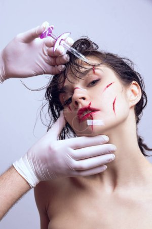 Young woman with scratches on face doing facial injection in cosmetological clinic. Fillers on face, syringe on forehead. Anti-wrinkles. Beauty standards, plastic surgery, health, cosmetology concept
