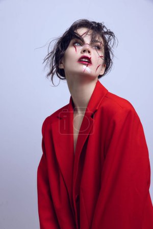 Portrait of beautiful young woman with red scratches on face, wearing red jacket and looking upwards. Concept of modern beauty standards, plastic surgery, health, cosmetology