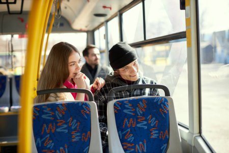 Photo for Friends, young man and woman sitting on modern tram with blurred passenger and city background. Cheerful talk. Transportation. Concept of public transport, urban lifestyle - Royalty Free Image