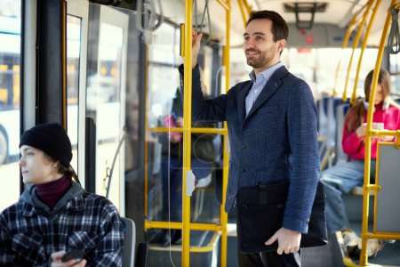 Photo for Focus on smiling man in jacket using public transport, modern tram for transportation. Blurred people on background. Concept of public transport, urban lifestyle - Royalty Free Image