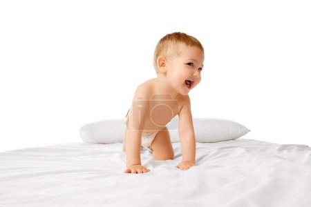 Photo for Happy little baby boy in diaper playing on bed, crawling, smiling isolated over white studio background. Concept of childhood and family, care, parenthood, infancy and heath - Royalty Free Image