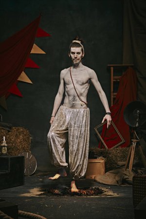Photo for Pale man with muscular shirtless body, yogi male circus performance over dark retro circus backstage background. Concept of circus, theater, performance, show, retro and vintage - Royalty Free Image