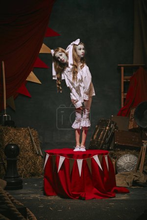 Siamese twin girls in white vintage costumes with makeup standing over dark retro circus backstage background. Creative spooky play. Concept of circus, theater, performance, show, retro and vintage