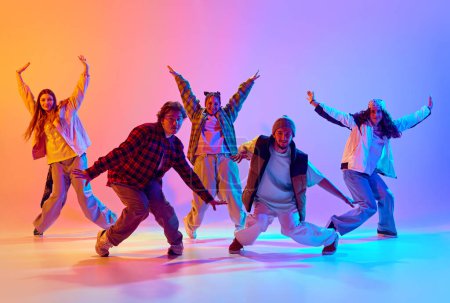 Dynamic image of young people, men and women in casual clothes dancing contemp against gradient studio background in neon light. Concept of modern dance style, hobby, active lifestyle, youth culture