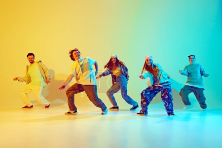 Téléchargez les photos : Performance dynamique de cinq danseurs talentueux en mouvement, dansant la danse moderne sur fond jaune vert dégradé sous la lumière du néon. Concept de style de danse moderne, passe-temps, mode de vie actif, culture des jeunes - en image libre de droit
