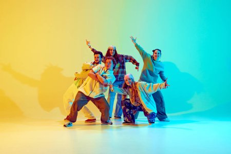 Téléchargez les photos : Diverses personnes, danseurs en vêtements décontractés colorés, debout en pose sautante dynamique, performant sur fond vert jaune dégradé au néon. Concept de style de danse moderne, mode de vie actif, jeunesse - en image libre de droit