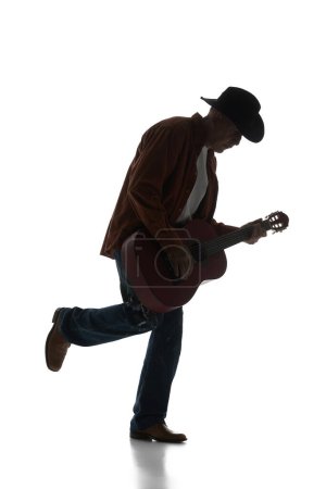 Foto de Silueta de hombre en sombrero fedora tocando la guitarra, actuando aislado sobre fondo blanco. Imagen en blanco y negro. Concepto de música, festival, concierto, entretenimiento, instrumentos. Póster, anuncio - Imagen libre de derechos