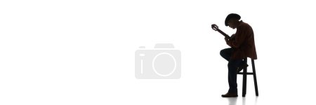Foto de Hombre en sombrero fedora sentado en la silla y tocando la guitarra sobre fondo blanco. Imagen en blanco y negro. Concepto de música, festival, concierto, entretenimiento, instrumentos. Banner, espacio vacío para el anuncio - Imagen libre de derechos