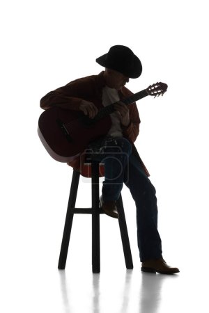 Foto de Hombre en sombrero fedora sentado en la silla y tocando la guitarra sobre fondo blanco. Imagen en blanco y negro. Artista en solitario. Concepto de música, festival, concierto, entretenimiento, instrumentos. Póster, anuncio - Imagen libre de derechos