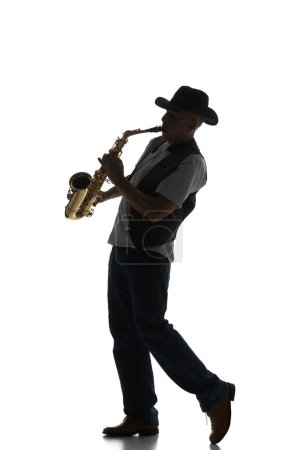 Téléchargez les photos : Silhouette d'homme en costume classique jouant du saxophone isolé sur fond blanc. Image en noir et blanc. Concept de musique, festival, concert, divertissement, instruments. Affiche, annonce - en image libre de droit