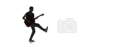 Téléchargez les photos : Silhouette d'homme jouant joyeusement de la guitare isolée sur fond blanc. Image en noir et blanc. Concept de musique, festival, concert, divertissement, instruments. Bannière, espace vide pour la publicité - en image libre de droit