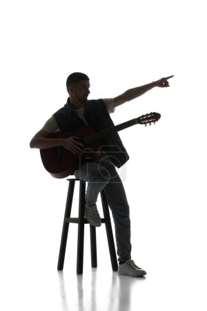 Photo for Artistic solo perfumer. Man sitting on chair with guitar isolated over white background. Black and white image. Concept of music, festival, concert, entertainment, instruments. Poster, ad - Royalty Free Image