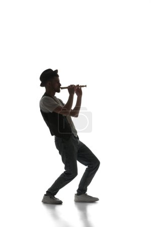 Téléchargez les photos : Silhouette masculine, jeune musicien talentueux jouant de la flûte isolée sur fond blanc. Image en noir et blanc. Concept de musique, festival, concert, divertissement, instruments. Affiche, annonce - en image libre de droit