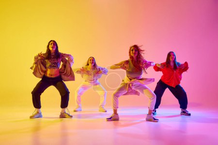 Four artistic young women in sport style casual clothes in motion, dancing freestyle dance against gradient background in neon. Concept of youth, street dance, contemporary dance, modern, dynamics