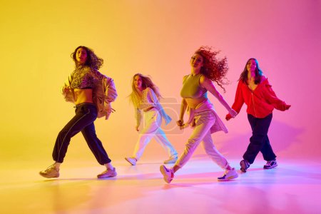 Téléchargez les photos : Quatre jeunes femmes artistiques dans des vêtements décontractés de style sportif en mouvement, dansant la danse freestyle sur fond dégradé au néon. Concept de jeunesse, danse de rue, danse contemporaine, moderne, dynamique - en image libre de droit
