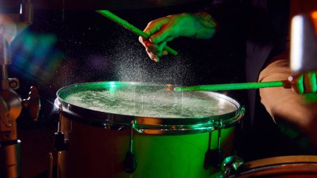Photo for Male hand playing drum with stick on dark background with green hued smoke and light flares. Concept of music, instruments, concert, sound, equipment, festival - Royalty Free Image