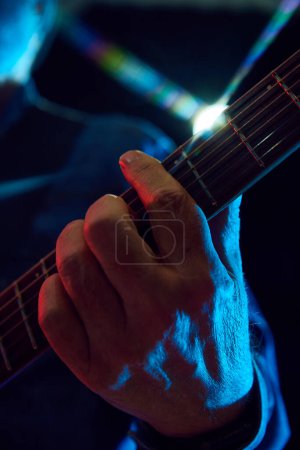 Foto de Primer plano de manos masculinas tocando la guitarra sobre fondo oscuro. Actuación acústica. Concepto de música, instrumentos, concierto, sonido, equipo, festival - Imagen libre de derechos