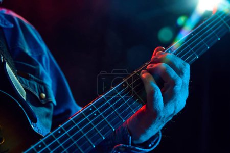 Photo for Focus on male hands, musician playing guitar against dark background with lights element. Poster for live event, solo performer . Concept of music, instruments, concert, sound, equipment, festival - Royalty Free Image
