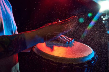 Photo for Close-up of male hands, musician playing bongo drums on dark background with stage lights. African culture live event. Concept of music, instruments, concert, sound, equipment, festival - Royalty Free Image