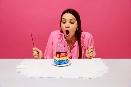 Photo for Young woman in pink shirt sitting at table with birthday cake made of dishwashing sponges, making birthday wishes and blowing candle. Concept of food pop art photography, creativity, quirky style - Royalty Free Image