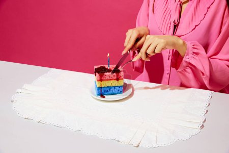 Téléchargez les photos : Image recadrée d'une femme en chemise rose assise à table et coupant un gâteau d'anniversaire fait d'éponges à vaisselle et de bougie. Fête d'anniversaire. Concept de cuisine pop art photographie, créativité, style décalé - en image libre de droit