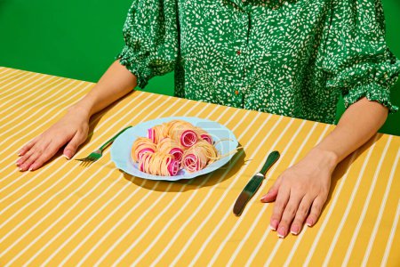 Photo for Creative representation of tasty dig. Spaghetti with hair curlers like sausages on yellow tablecloth with woman sitting on green background. Food pop art photography, creativity, quirky style concept - Royalty Free Image