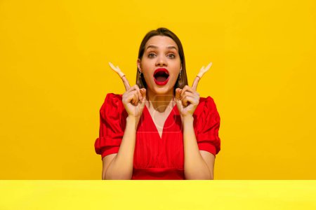 Photo for Woman in red dress with surprised expression, pointing upwards with toy hands against yellow background. Human emotions. Concept of food pop art photography, creativity, quirky style - Royalty Free Image