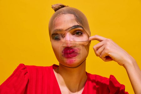 Junge Frau mit Strumpf über dem Kopf und verschmiertem Lippenstift-Make-up vor gelbem Hintergrund. Nahaufnahme. Geheimnisse. Konzept der Food-Pop-Art-Fotografie, Kreativität, skurriler Stil