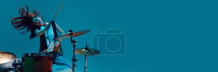 Photo for Artistic and energetic young woman, musician playing drums against cyan background in neon light. Concept of music, talent show, performance, concert, festival, instruments. Banner, ad - Royalty Free Image