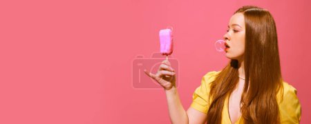 Foto de Mujer pelirroja Yong sosteniendo helado falso hecho de jabón y haciendo burbuja de jabón con la boca contra el fondo rosa. Concepto de fotografía pop art, creatividad. Banner. Espacio vacío para el anuncio - Imagen libre de derechos