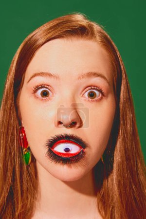 Schockierte Frau mit Augen-Make-up auf den Lippen vor grünem Hintergrund. Psychologischer Thriller über Selbstwahrnehmung und Identität. Konzept der Pop-Art-Fotografie, Kreativität, Surrealismus, Horror, skurril