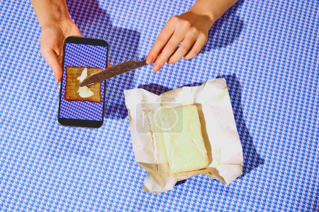 Photo for Hands buttering virtual toast on a smartphone screen with real butter and knife. Ad for a cooking app showcasing interactive and digital recipe tutorials. Concept of pop art photography, creativity - Royalty Free Image