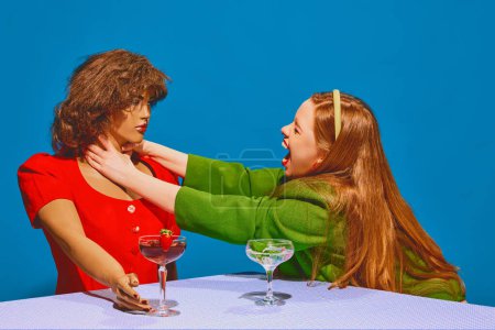 Téléchargez les photos : Jeune femme rousse assise à table avec mannequin et exprimant des émotions stressantes sur fond bleu. Concept de photographie pop art, créativité, psychologie, communication - en image libre de droit