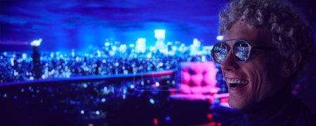 Foto de Feliz joven parado al aire libre por la noche. Gafas que reflejan fuegos artificiales y luces de la ciudad. Concepto de estilo de vida urbano, vacaciones, emociones humanas. Banner - Imagen libre de derechos