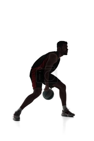 Foto de Silueta de hombre, jugador de baloncesto en movimiento durante el juego, bola de drible, entrenamiento aislado sobre fondo blanco. Concepto de deporte profesional, competición, juego, torneo, acción - Imagen libre de derechos
