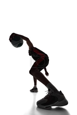 Photo for Silhouette of young man, basketball player in motion, training, playing, dribbling ball isolated on white background. Concept of professional sport, competition, game, tournament, action - Royalty Free Image