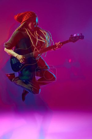 Foto de Imagen dinámica del joven artístico, músico tocando la guitarra sobre fondo rosa en neón con efecto de luces mixtas. Festival de música Reggae. Concepto de música, performance, arte, concierto - Imagen libre de derechos