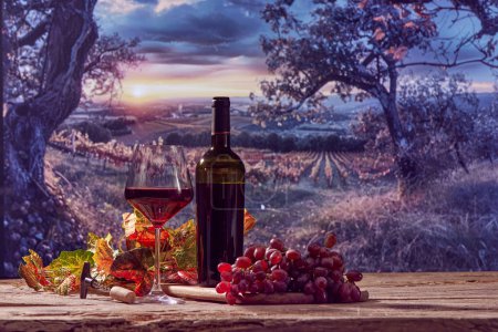 Téléchargez les photos : Bouteille de vin, verre avec vin rouge, grappe de raisin, feuilles de vigne sur table en bois avec beau paysage naturel. Concept de vinification, boisson bio, nature, traditions - en image libre de droit