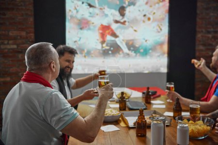 Photo for Friends coming together to watch an online football match on TV, with beer and snacks adding to the enjoyment of the game. Concept of sport, championship, game, sport fans, leisure - Royalty Free Image