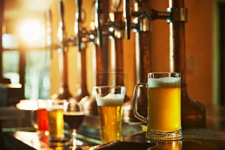 Photo for Glasses with various foamy beer tastes on wooden counter standing near beer taps. Modern bar, pub aesthetics. Concept of beer drink, alcohol, brewery, pub atmosphere, taste - Royalty Free Image