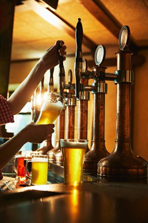 Téléchargez les photos : Barman versant de la bière blonde mousseuse dans le verre du robinet, intérieur du pub. Profiter d'une boisson fraîche. Concept de boisson à la bière, alcool, brasserie, ambiance pub, goût - en image libre de droit