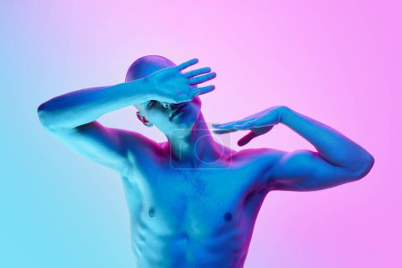 Foto de Retrato de un joven calvo sin camisa posando con gestos sobre fondo rosa degradado en luz de neón. Concepto de belleza masculina, cuerpo, juventud, fitness, deporte, salud - Imagen libre de derechos