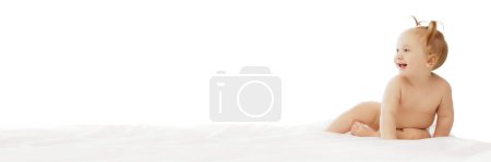 Téléchargez les photos : Joyeux sourire petite fille en couches assise dans le lit avec une expression heureuse isolée sur fond blanc. Bannière. Concept d'enfance, soins, santé, bien-être, parentalité - en image libre de droit