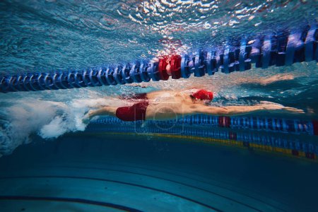 Photo for Muscular young man, swimmer in motion, preparing for competition, training in swimming pool indoors. Speed and technique. Concept of professional sport, health, endurance, strength, active lifestyle - Royalty Free Image