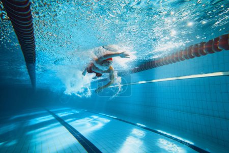 Téléchargez les photos : Image dynamique du jeune homme, nageur en mouvement, nageur acrobatique dans la piscine, entrainement. Concept de sport professionnel, santé, endurance, force, mode de vie actif - en image libre de droit